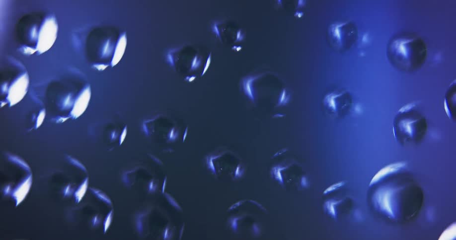 Blue light shines on water droplets as texture is reflected inside from the moving light