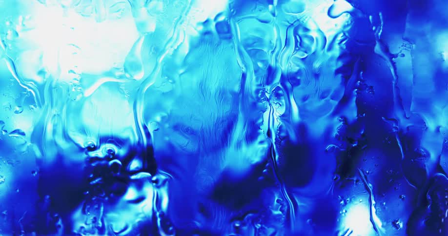 Water droplets drip down clear glass as blue lights shine and reflect on the droplets
