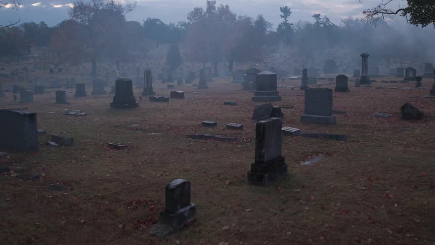 Leaves litter the ground of an old cemetery on a foggy fall evening