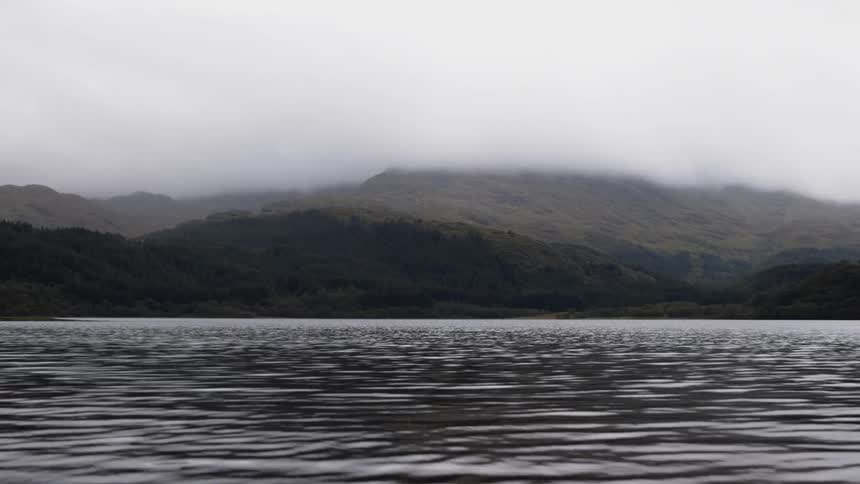 Water flows away from misty hills on shore on overcast day