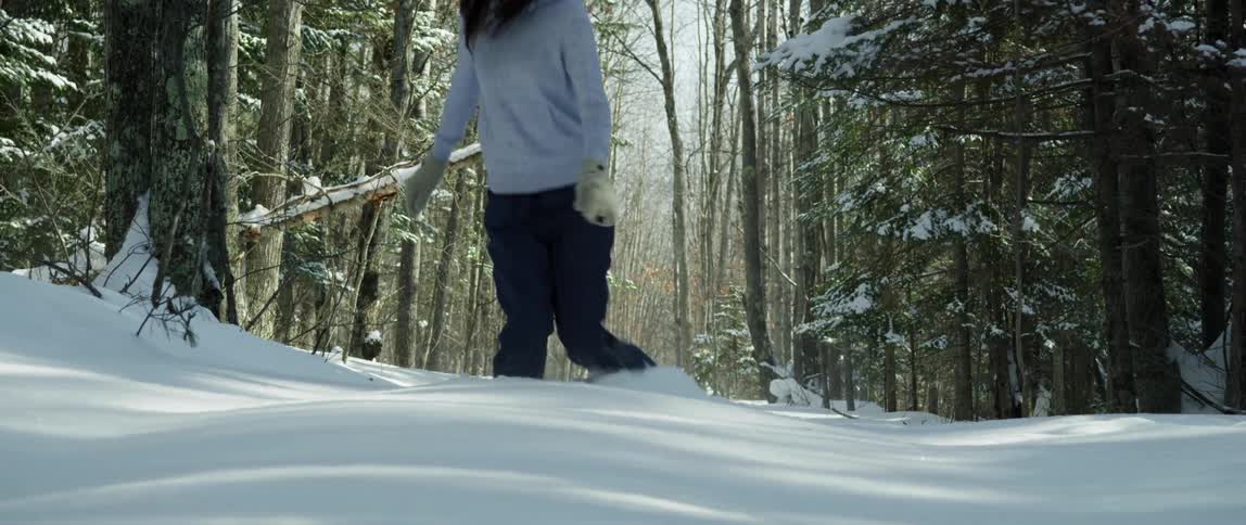 A young woman is snowshoeing up a hill in deep snow and a surrounding forest
