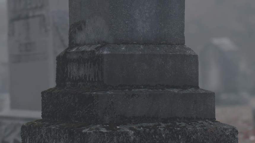 A headstone stands in a foggy cemetery