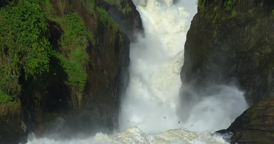 A huge waterfall crashes into the water between two cliffs growing moss