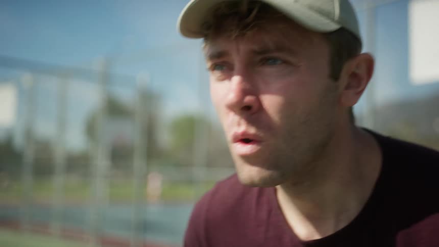 Tennis player plays on court as people behind him play other ballgames on separate sports courts