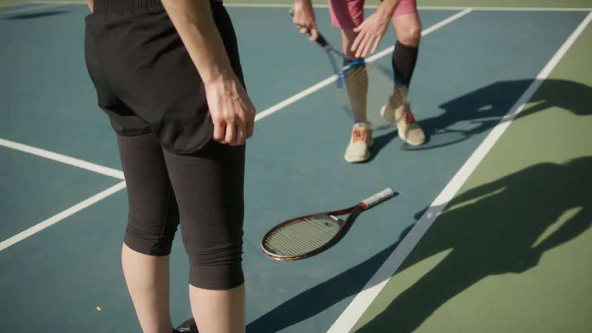 A woman tries to spin her racket on a tennis court as a friend watches