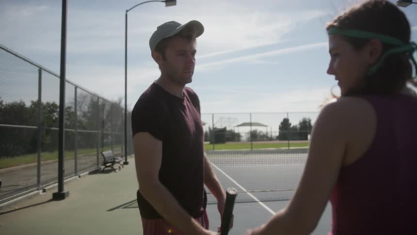 Man and woman exchange tennis rackets before playing tennis