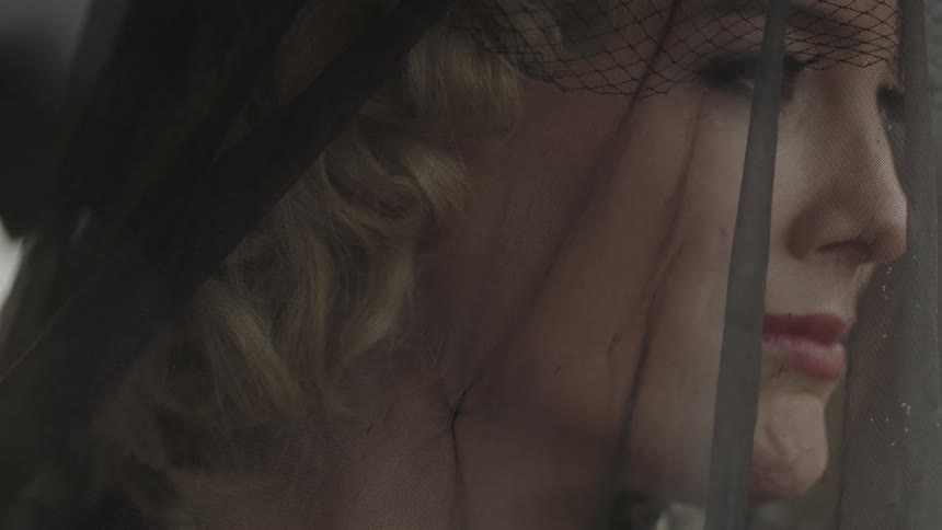 A woman wearing a lace hat mourns on a rainy day