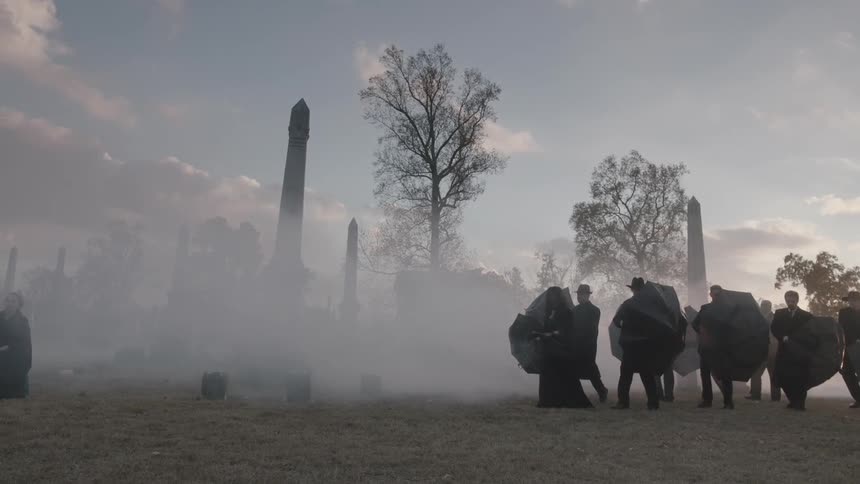 People walk through a foggy cemetery
