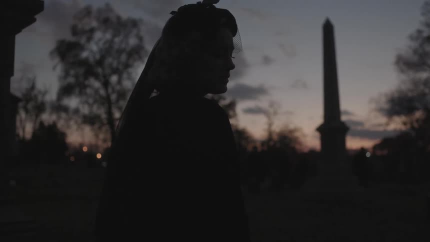 A woman stands in a windy cemetery at dawn