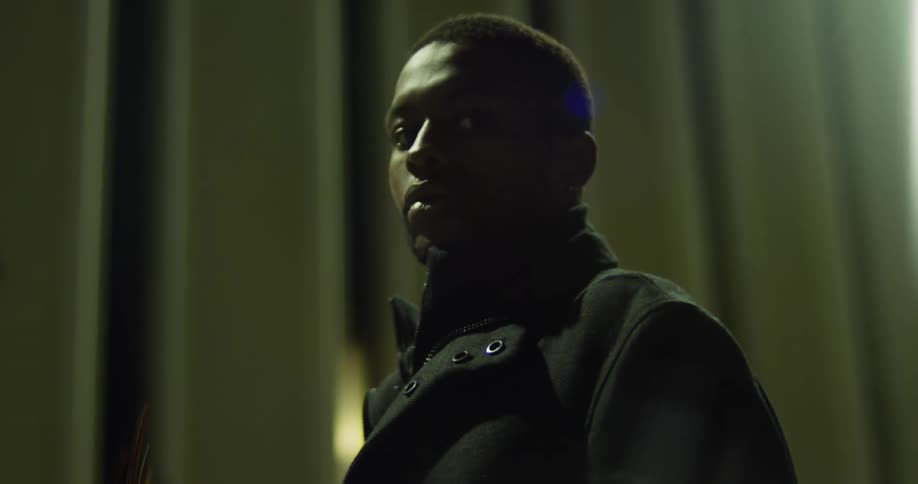 Black man wearing black overcoat looking at camera removes sunglasses