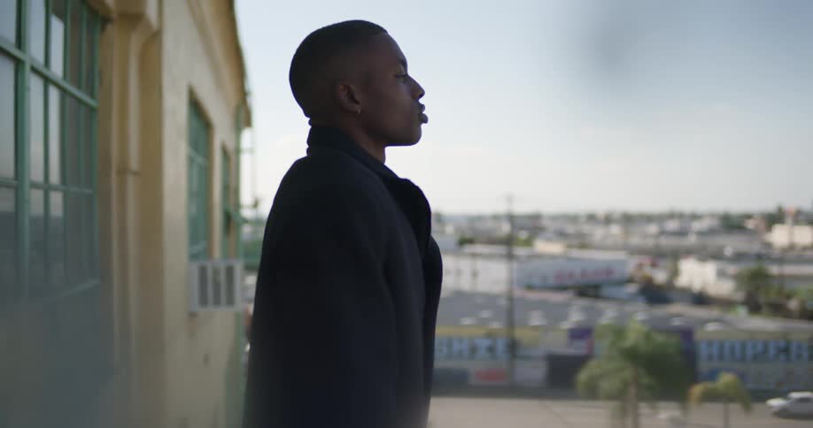A man dressed in black stands outside a house looking forward in front of a neighborhood