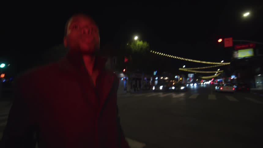 Man crosses city street at night as cars wait at traffic light