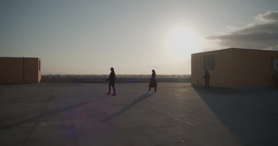 Three people walk across area between buildings under a sunny sky