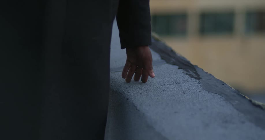 A man runs his hand along the edge of a building rooftop