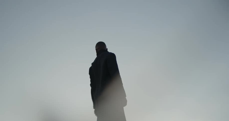 Man standing on a rooftop pointing at the cloudy sky birds are flying by at sunrise