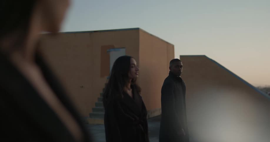 Man and woman stare at each other across the woman standing between them near building
