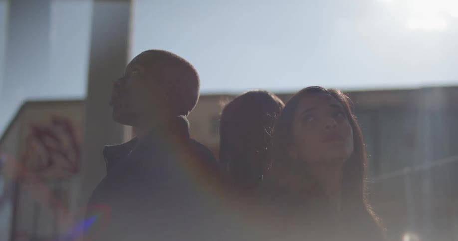 A man and two women standing with the backs to each other under a highway bridge on a sunny day looking up