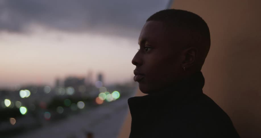 A man standing with his back against a wall staring out into the distance as cars go by