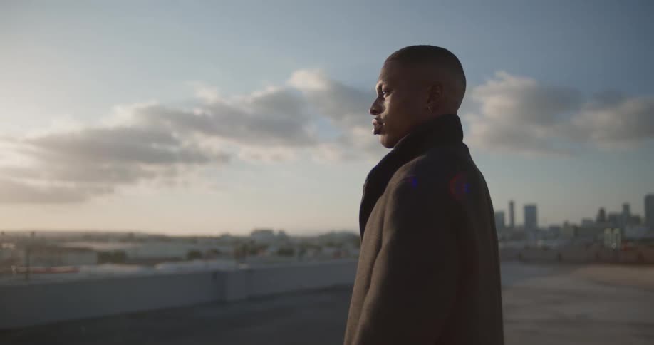 Shaved head man in black coat and woman in black jacket walks on top of building looking around