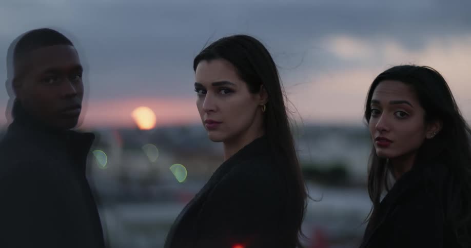 Three people turn around while standing on a rooftop