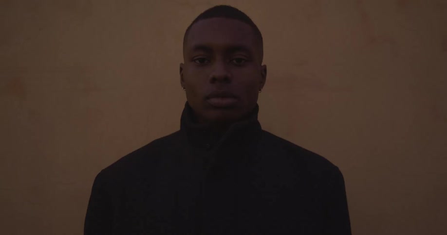 A man stands still in front of a wall as a light flashes