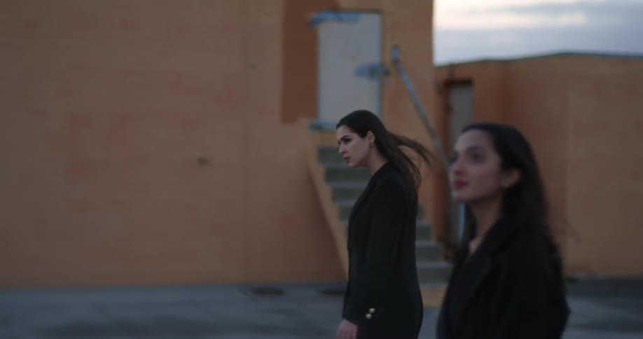 Two young women are walking in front of some unfinished looking houses and one woman looks up at the sky
