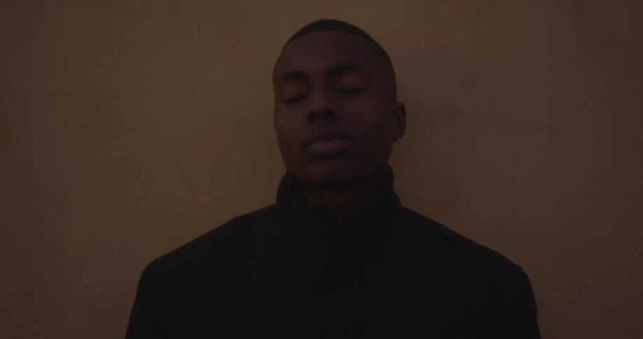 A man with his eyes closed standing against a wall