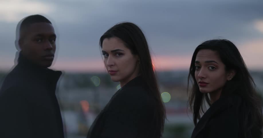 Trio stands in black coats against sun sitting on horizon