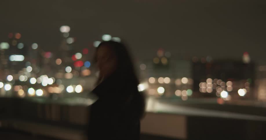 Woman walks across bridge overlooking city at night