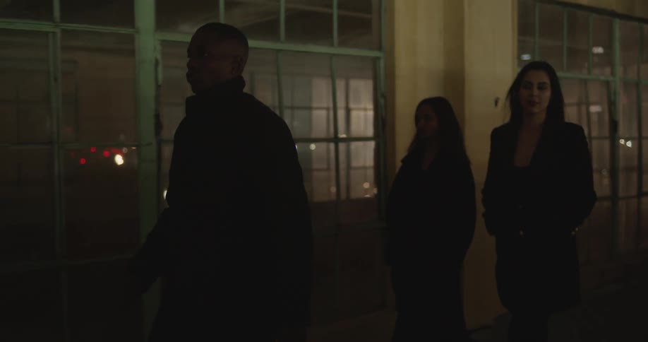 Man and women walk together past windows as light shines through from other side at night