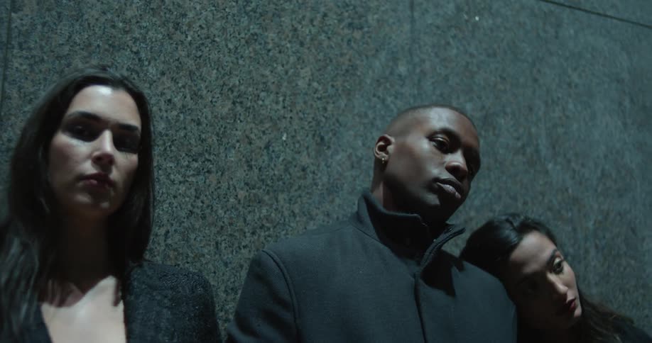 Two women and one man model in black near a granite wall