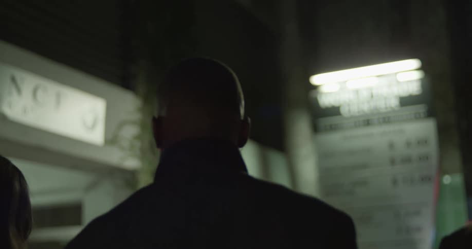 Man in black coat and women wearing black coat and blazer jacket walk down the street at night