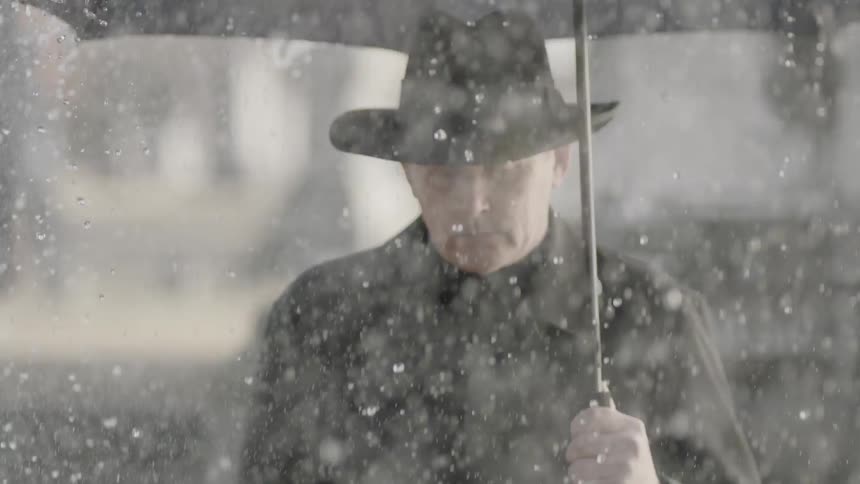 A man holding an umbrella mourns at a cemetery as rain falls