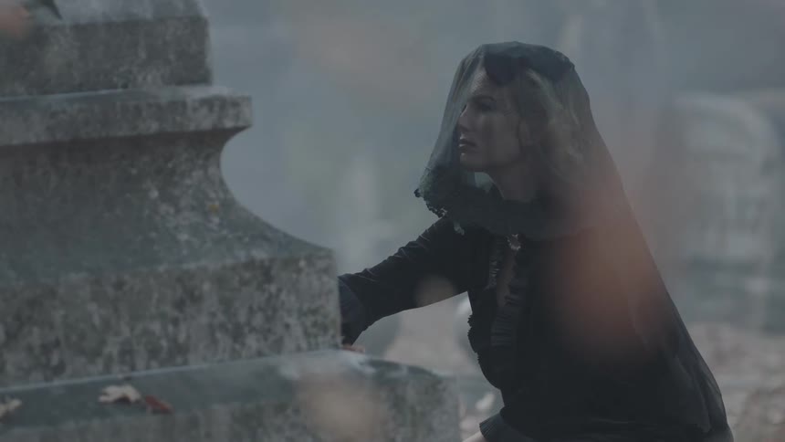A woman in black looks at a gravestone
