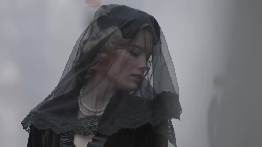 A woman in a black veil with leaves blowing around