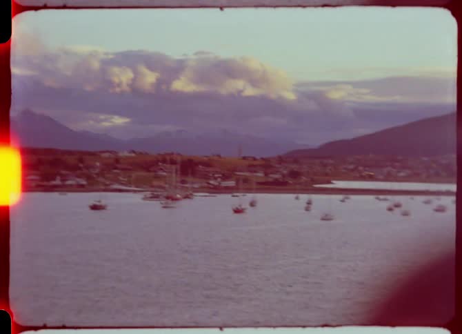 Panoramic view of a bay yachts and other boats floating in the ocean a city and mountains on a cloudy evening in the background
