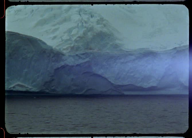 An iceberg floats in the artic water in front of a glacier