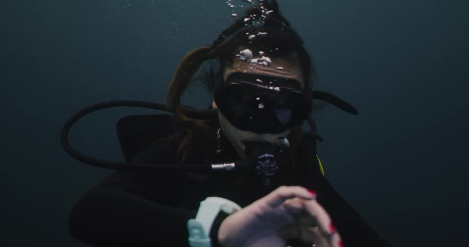 A woman diving underwater looks at her watch
