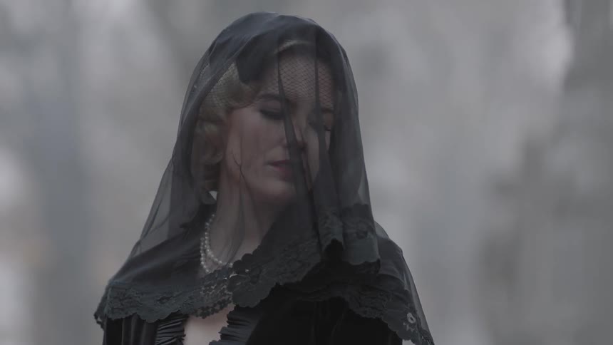 A woman is standing outside wearing a veil as leaves fall