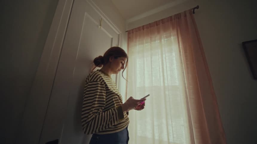 A woman is using her cell phone by the window