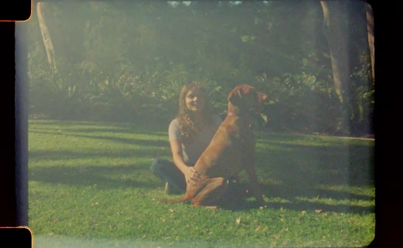 A woman is sitting on the grass with her dog whom she is petting and playing with
