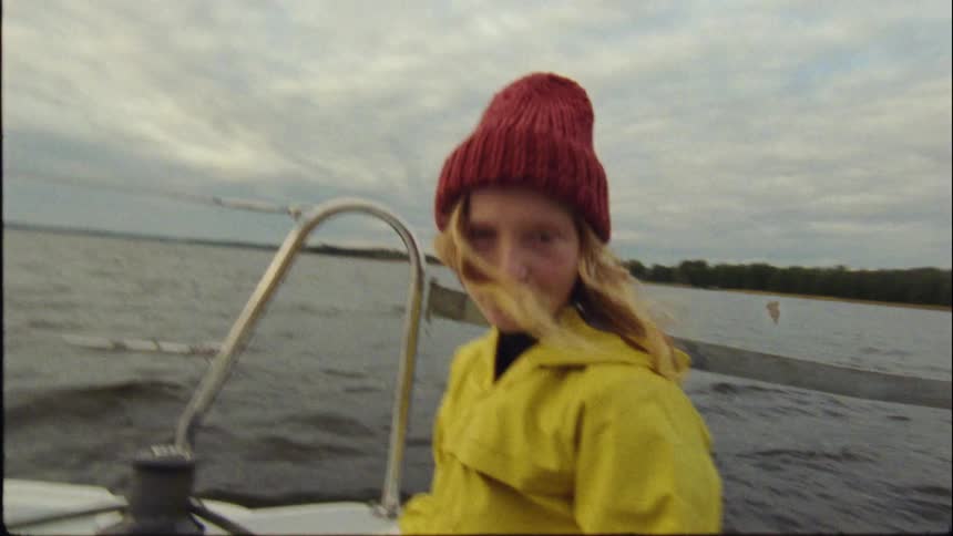 Woman wearing yellow raincoat stands in bobbing motorboat a short distance from the shore