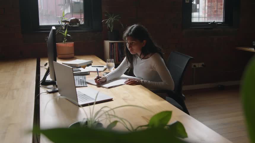 A woman takes notes while sitting at her computer desk