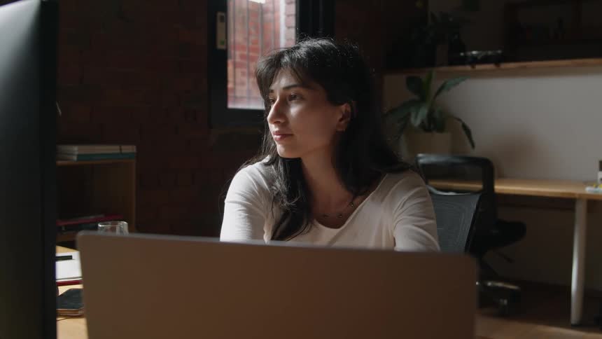 A woman is sitting down and typing on her laptop