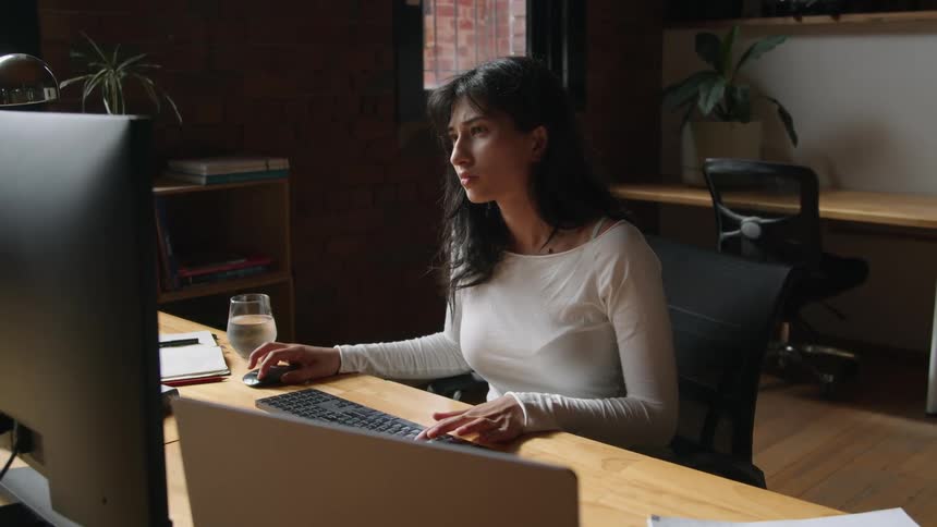 A woman is typing on a computer while sitting indoors