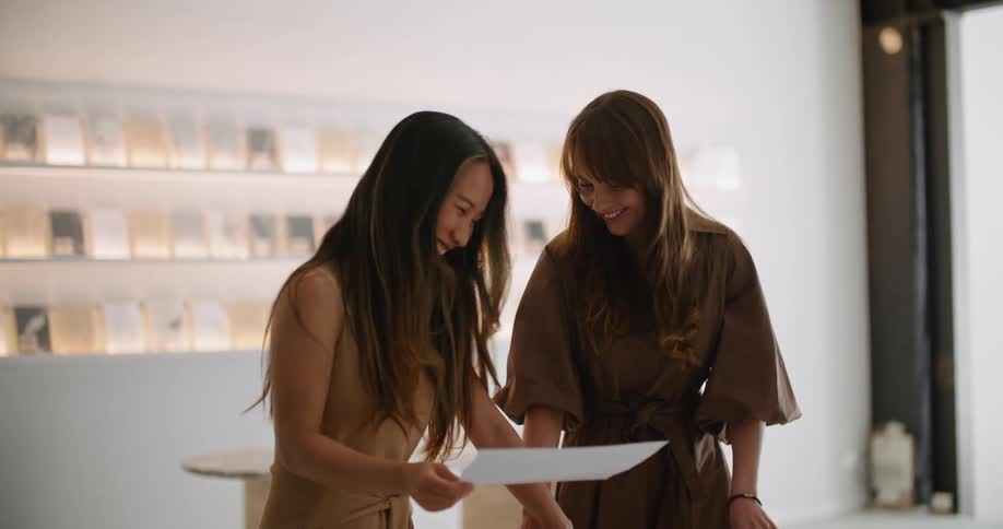 Two women in an office look at a piece of paper and laugh