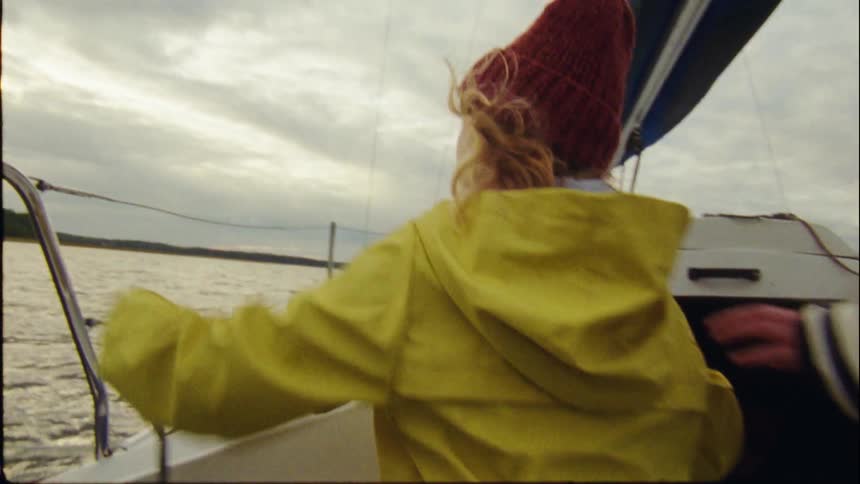 A child wearing a yellow coat unwraps rope on a boat while a woman stands near