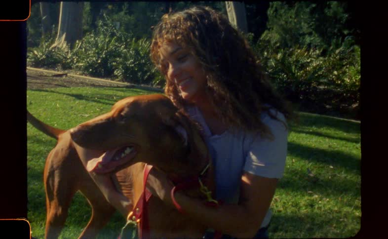 A young woman is kneeling on grass while petting and holding her dog