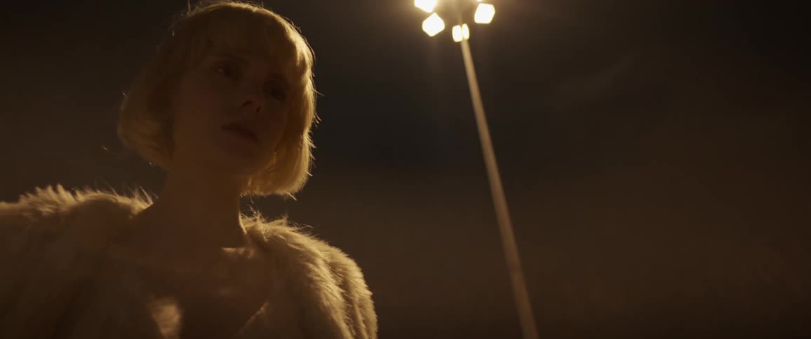 Blonde woman with short haircut stands against the light pole at night in the street