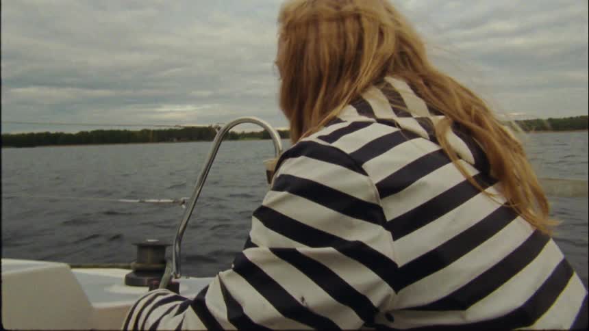 A woman in a striped coat wraps and tugs on rope on a baot